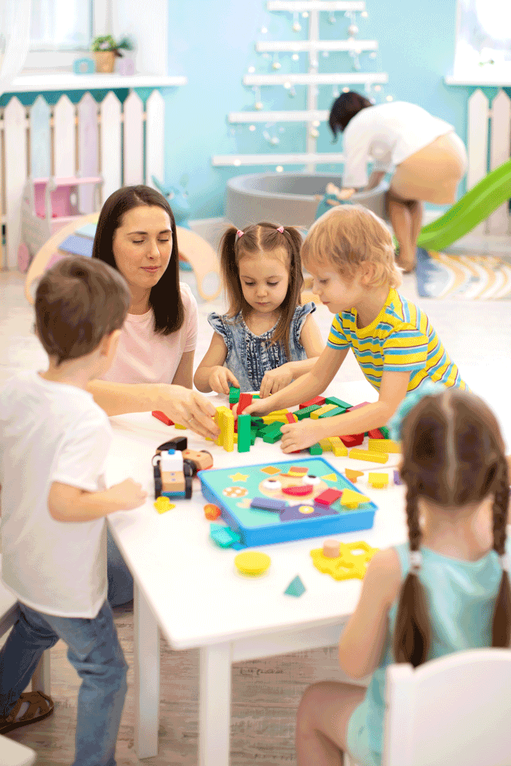 Educator helping kids playing with block constructor in daycare